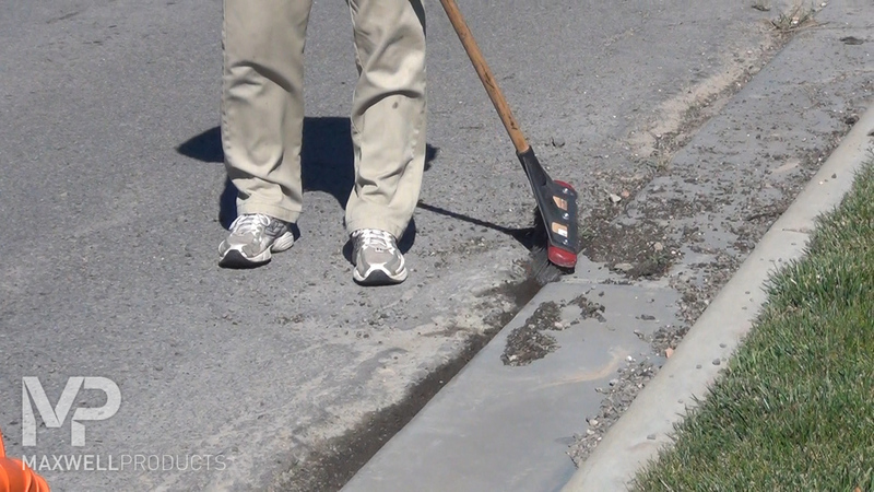 A road crew uses a wire broom to clean and remove loose pavement.