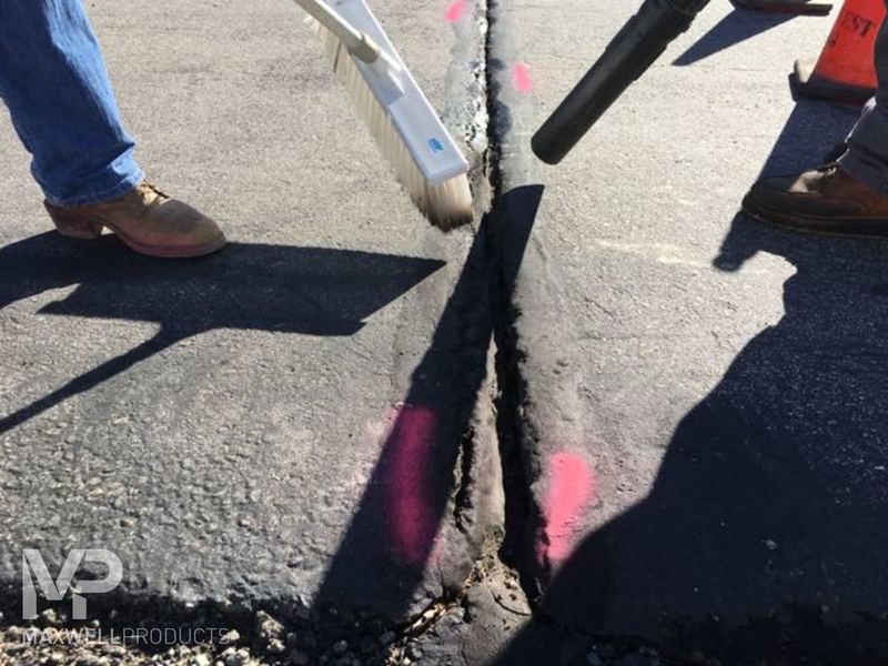 A road crew prepares a wide crack for GAP Mastic by cleaning it with a broom and blower.