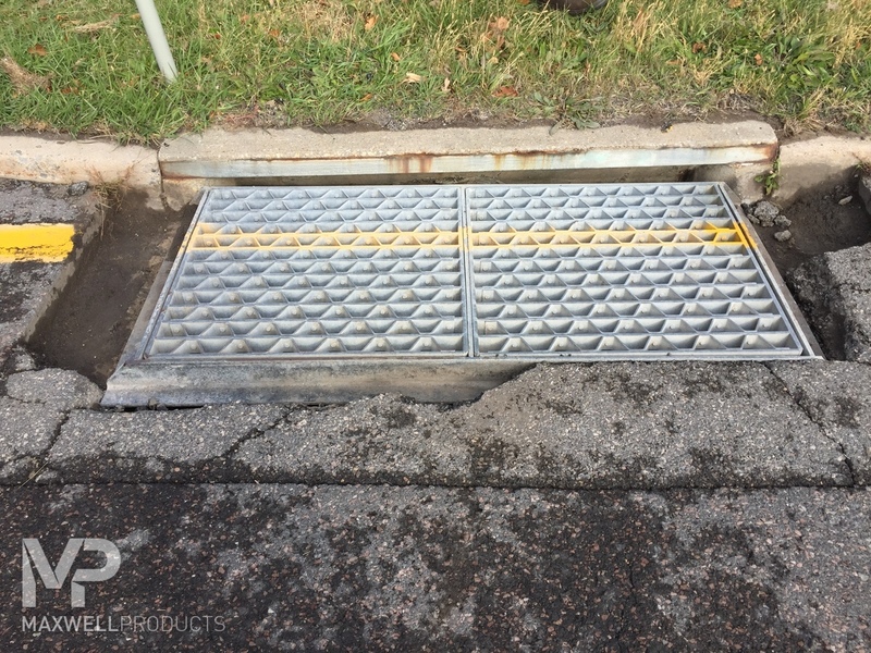 The pavement around a drain is deteriorating, cracking, and distressed.